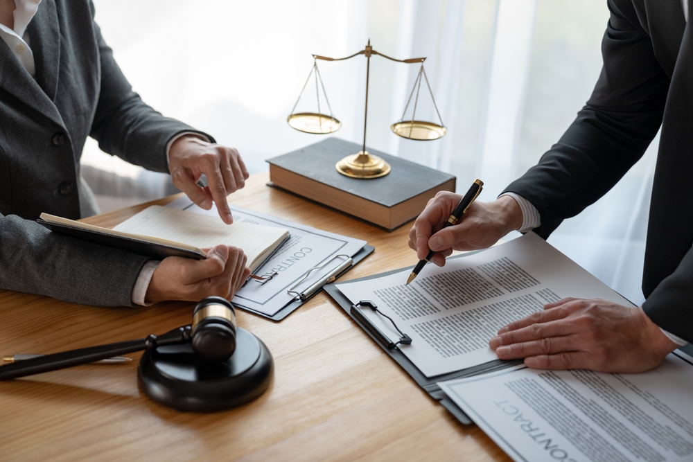 Lawyer reviewing and signing legal contract with client in law office with gavel and justice scales on desk. Lawyer reviewing and signing legal contract with client in law office with gavel and justice scales on desk.