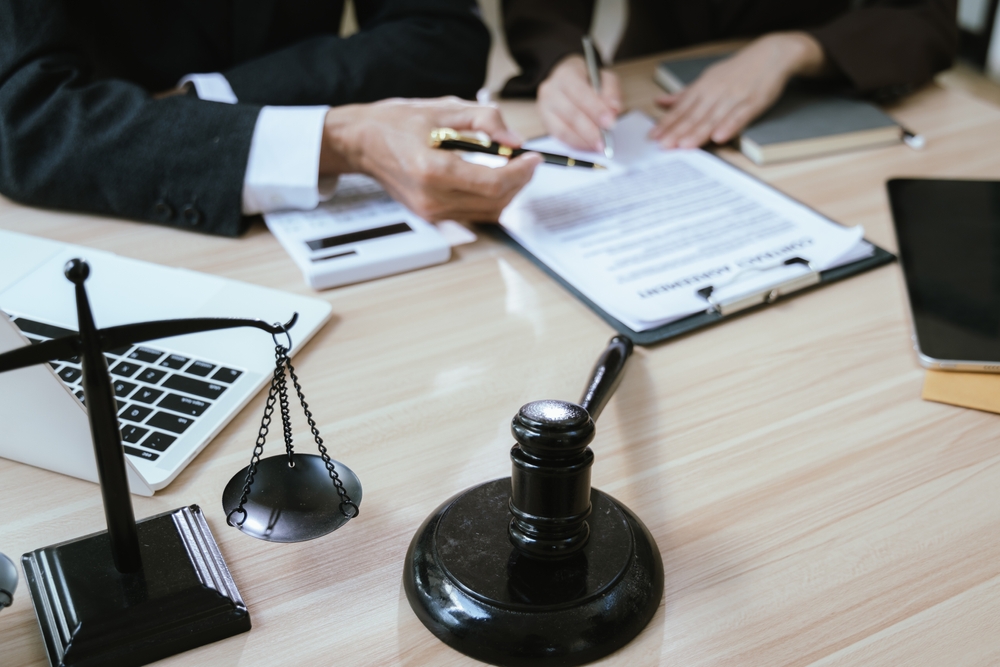 Lawyer and client reviewing legal agreement with gavel and justice scales on office desk. Lawyer and client reviewing legal agreement with gavel and justice scales on office desk.