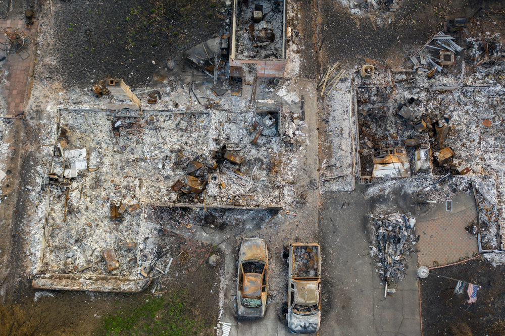 Aerial view of wildfire destruction showing burned vehicles and the remains of a residential property reduced to rubble and ash
