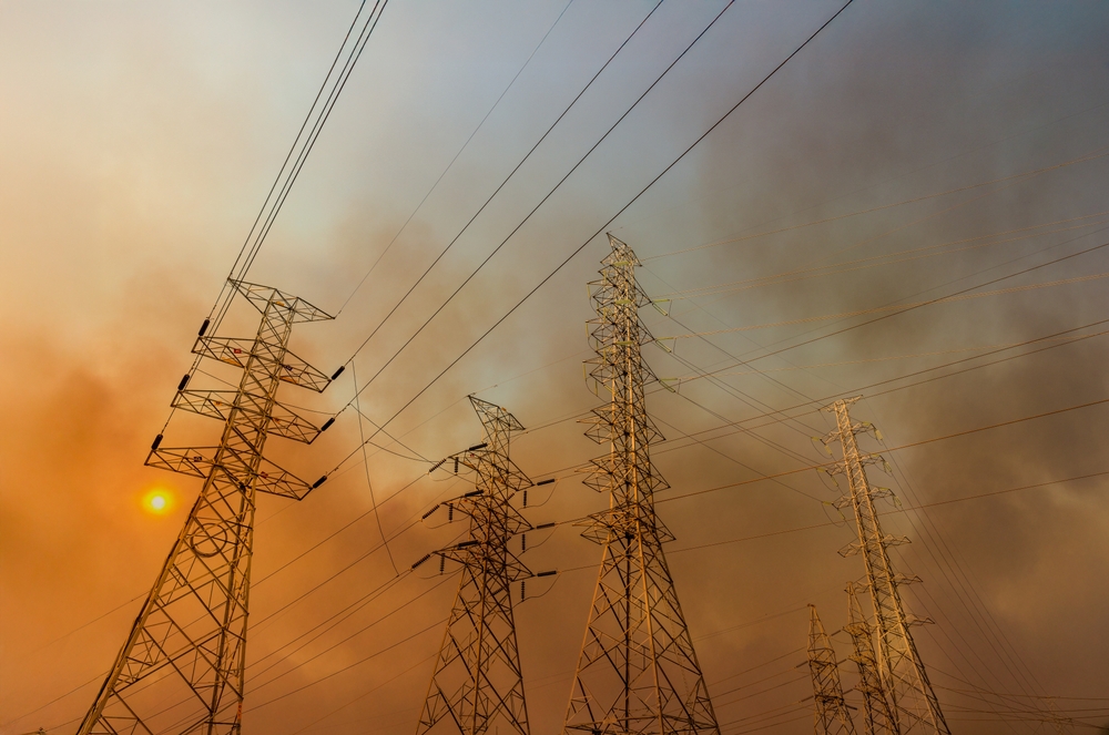 Utility power lines surrounded by wildfire smoke, highlighting potential corporate liability in fire cases.