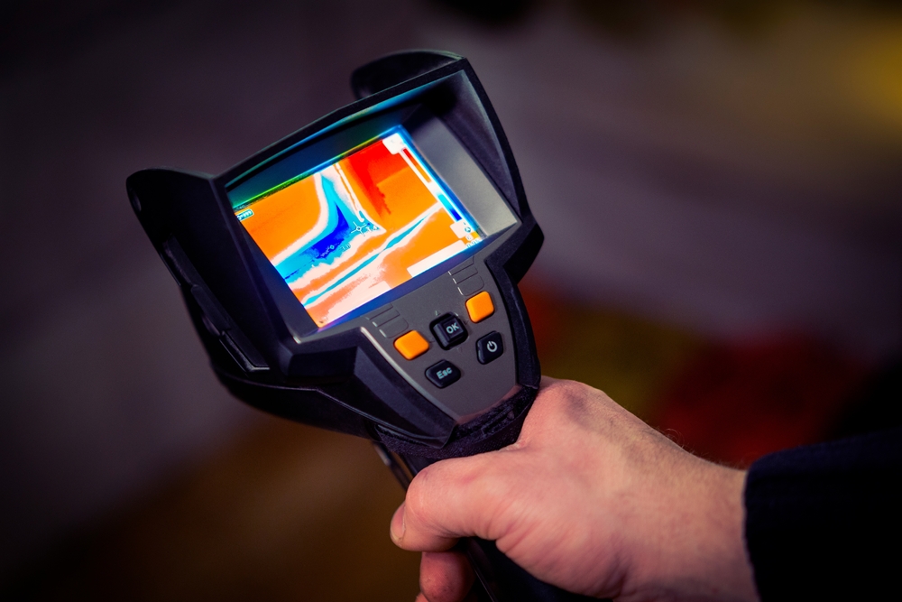 Hand holding a thermal imaging device displaying heat patterns for wildfire damage assessment.