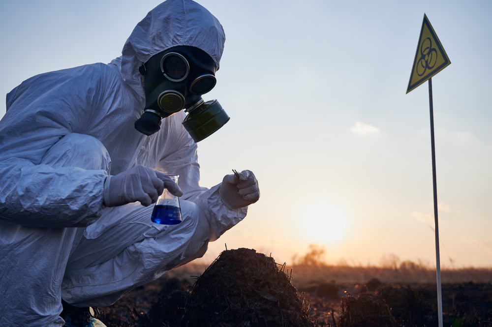 Industrial hygienist in protective suit and gas mask collecting soil samples after wildfire contamination